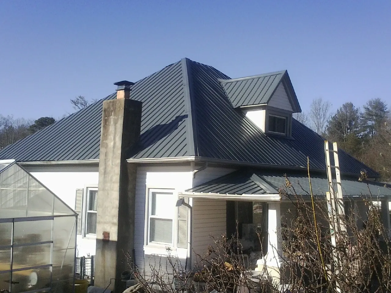 Dark blue standing seam metal roof on a white farmhouse with dormer — Slate & Tile Roof Repair by Roofing Brothers in Turney