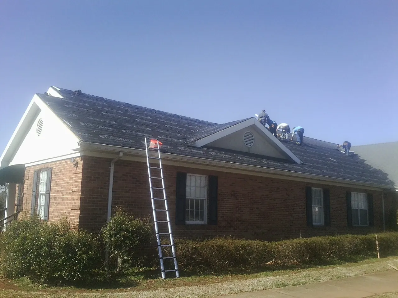 Crew tearing shingles off a brick ranch roof with a ladder set — Emergency Roof Repair work by our crew in Turney