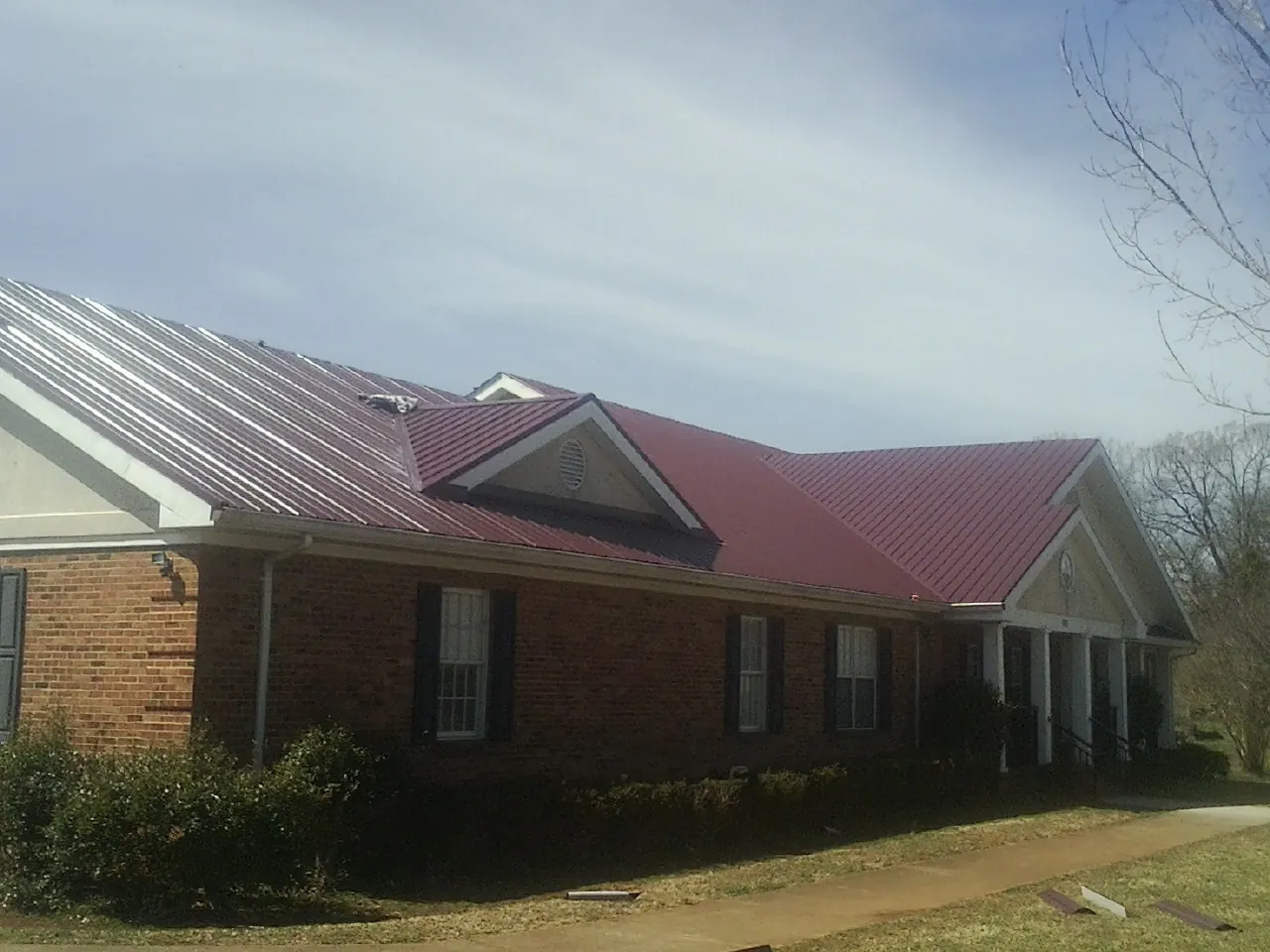 Red metal roof with gabled entries on a long brick building, from a Hail Damage Roof Repair job in Turney