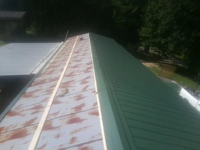 Old rusted panels beside newly installed green metal roofing — Wind Damage Roof Repair by Roofing Brothers in Turney