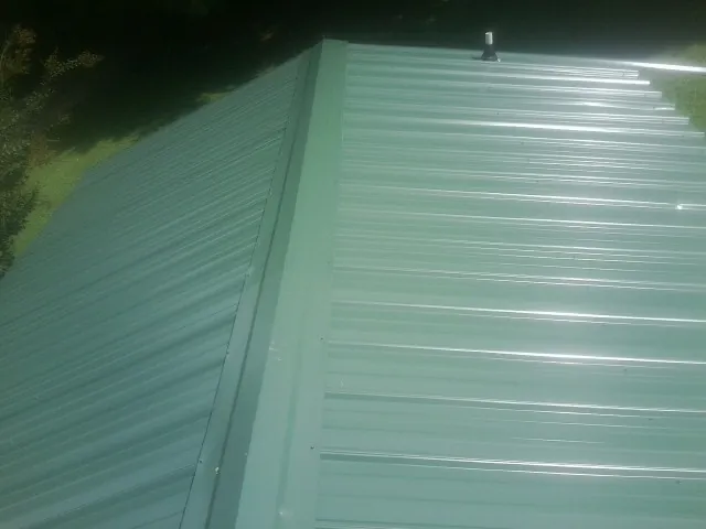 New green metal panels meeting at the ridge of a roof — Flat Roof Repair work by our crew in Turney