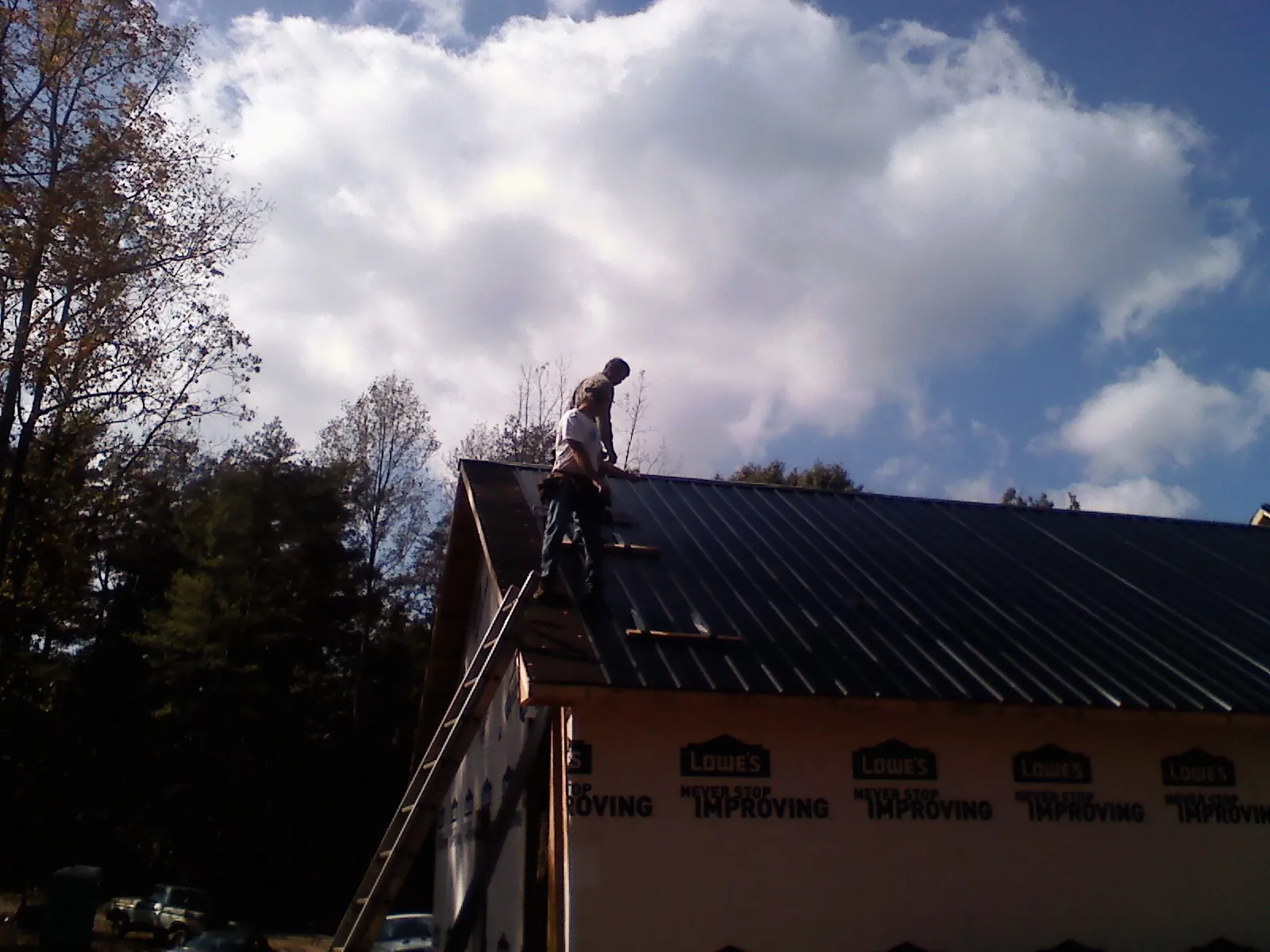 Roofer fastening dark metal panels high against a cloudy sky, from a Roof Inspection job in Turney