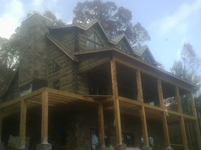 Stone chimney and dormers on a large log home with a timber porch in Turney